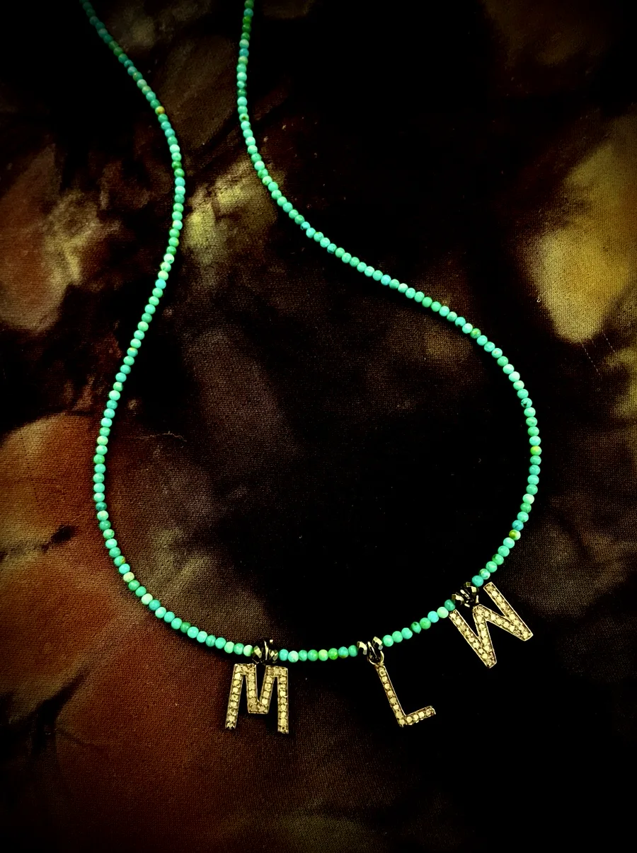 Turquoise initial charm lovebeads on dark fabric